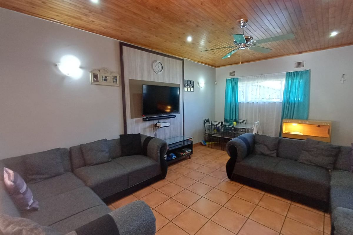 Spacious living room featuring a warm timber tongue and groove ceiling, ceramic tiled flooring, and a dedicated feature wall for media entertainment.