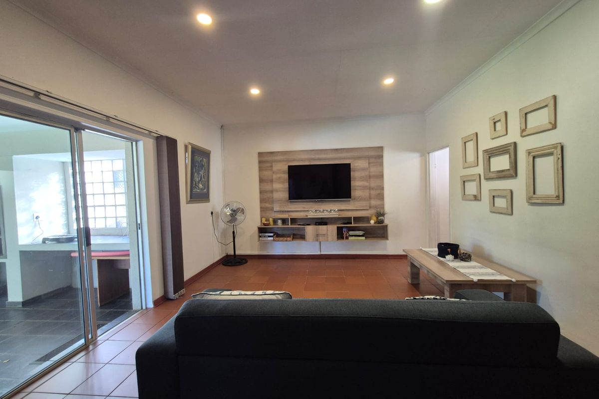 A well-maintained living room featuring tiled flooring, recessed downlights, and a built-in media console, with direct access to an outdoor patio area.