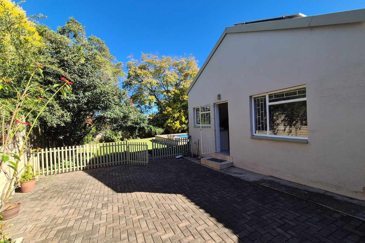 Rear exterior view featuring a paved patio area, security gates, and window bars, with access to the garden and pool area.