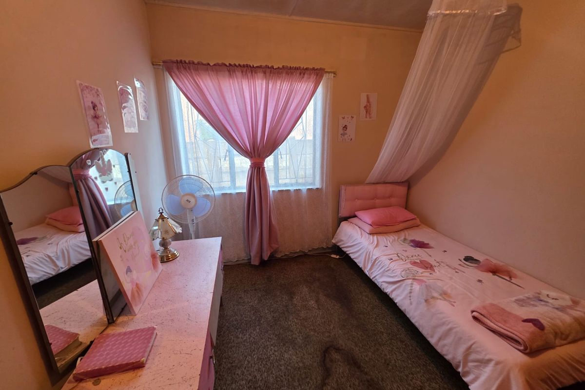 A compact bedroom featuring a window with security bars, carpeted flooring, and a ceiling showing signs of potential water staining.