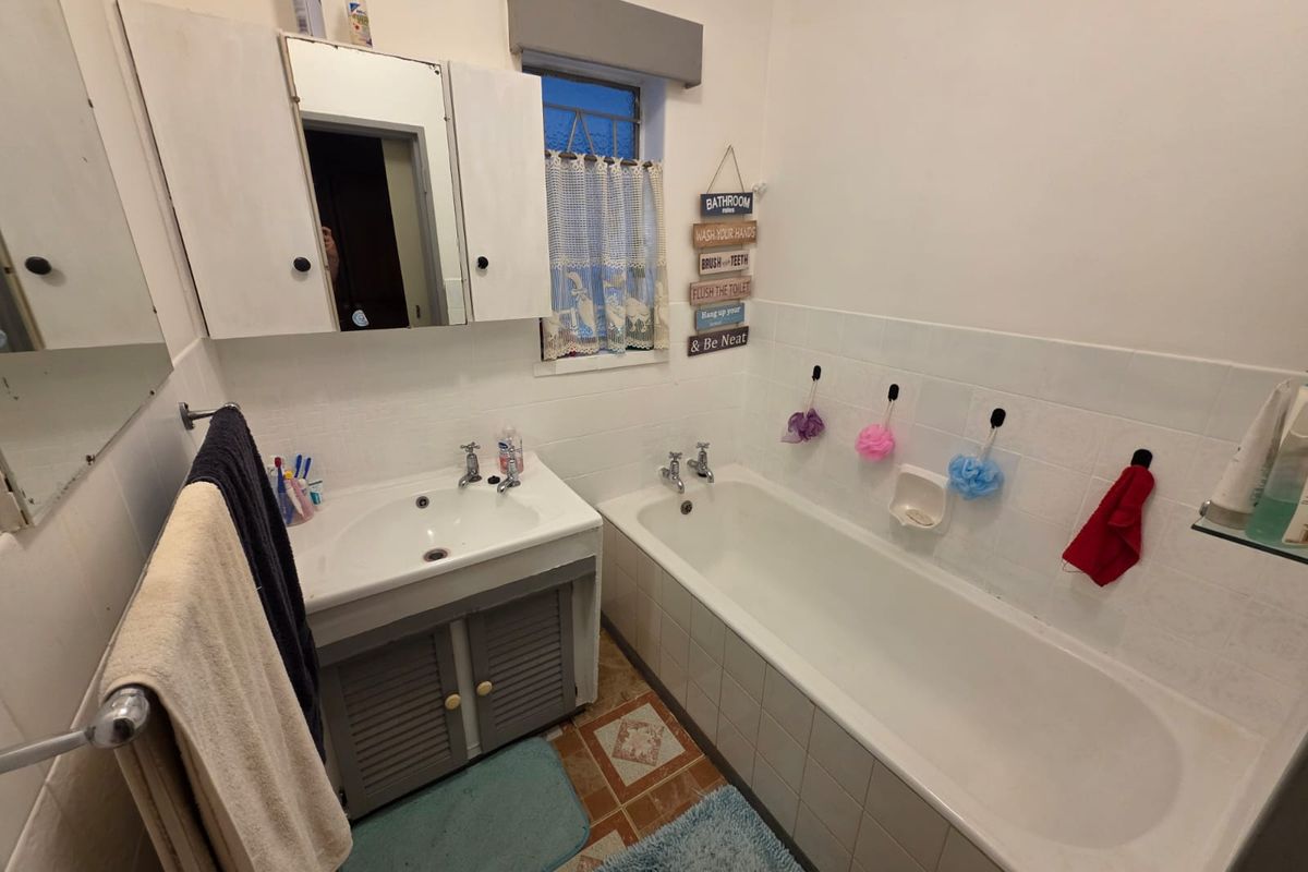 A functional bathroom featuring a built-in bathtub, vanity basin with storage cabinet, wall-mounted medicine cabinet, and tiled splashbacks.