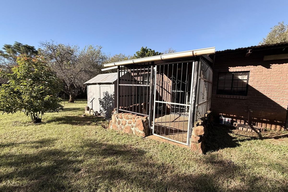 Rear exterior view showing a brick house facade with a metal-enclosed patio area, stone base, and a detached metal storage shed in the garden.