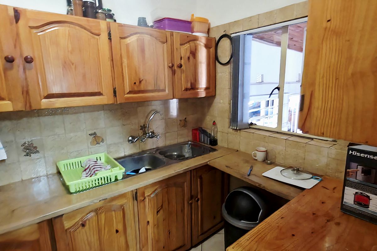 A compact kitchen featuring traditional wooden cabinetry, laminate countertops, and a double bowl stainless steel sink with a tiled splashback.