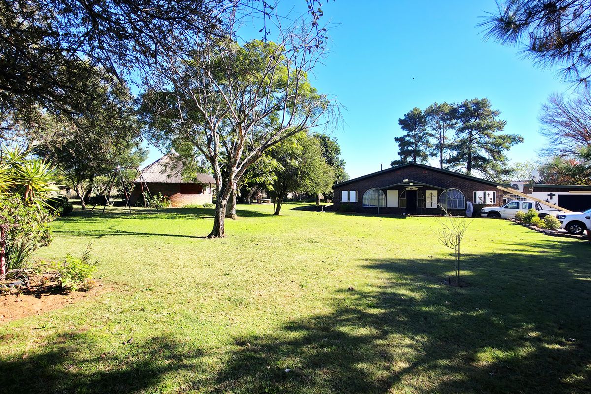 Spacious rear garden featuring a large lawn, mature trees, and a detached thatched lapa, providing ample outdoor space and a private setting.