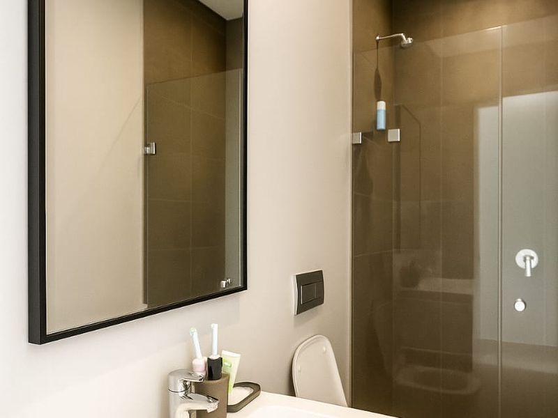 Modern bathroom featuring a sleek vanity with integrated basin, wall-mounted mirror, and a glass-enclosed walk-in shower with contemporary tiling.