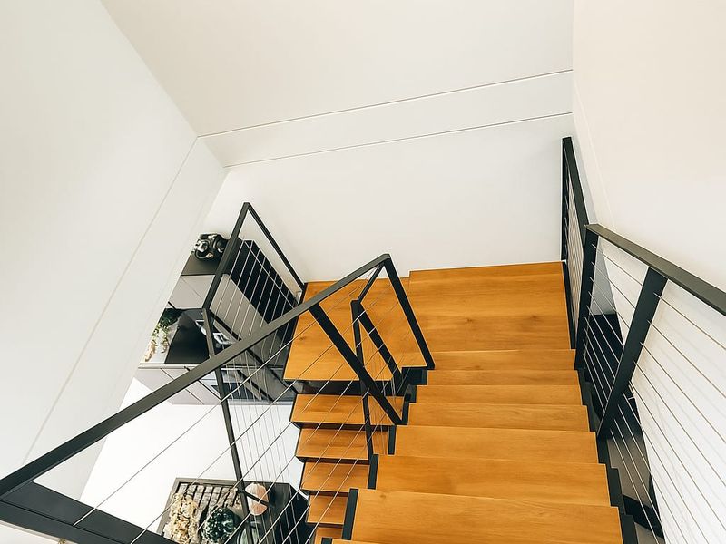 A modern staircase featuring timber treads and a sleek black metal balustrade with wire infill, viewed from an elevated perspective.