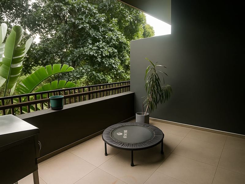 A covered balcony featuring tiled flooring, a metal railing, and a dark accent wall, offering a peaceful view of surrounding mature trees.