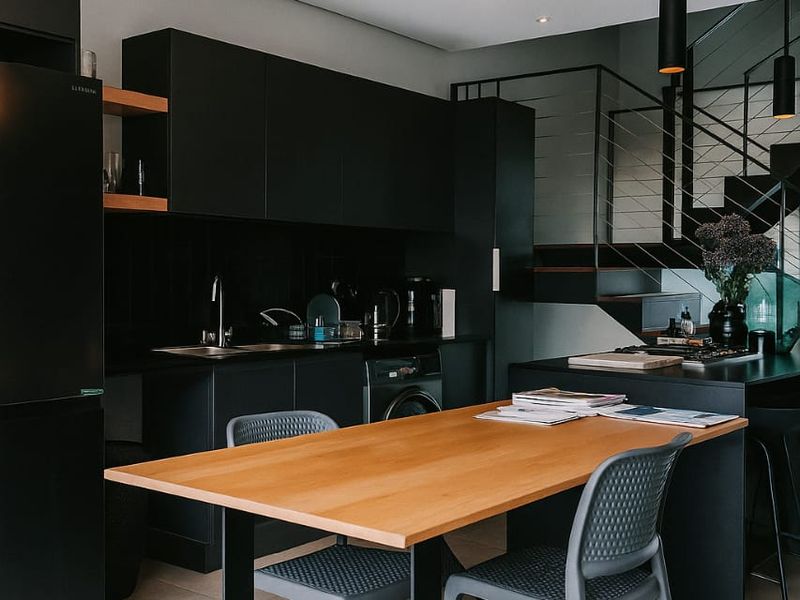 Modern open-plan kitchen featuring sleek matte black cabinetry, integrated appliances, a central island, and contemporary pendant lighting, seamlessly connected to the living area.