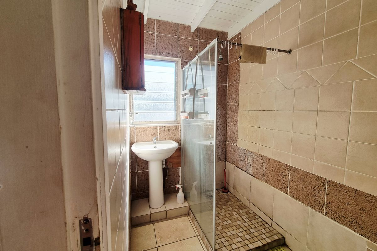A dated bathroom featuring a pedestal basin, a glass-enclosed shower, and tiled walls and flooring.
