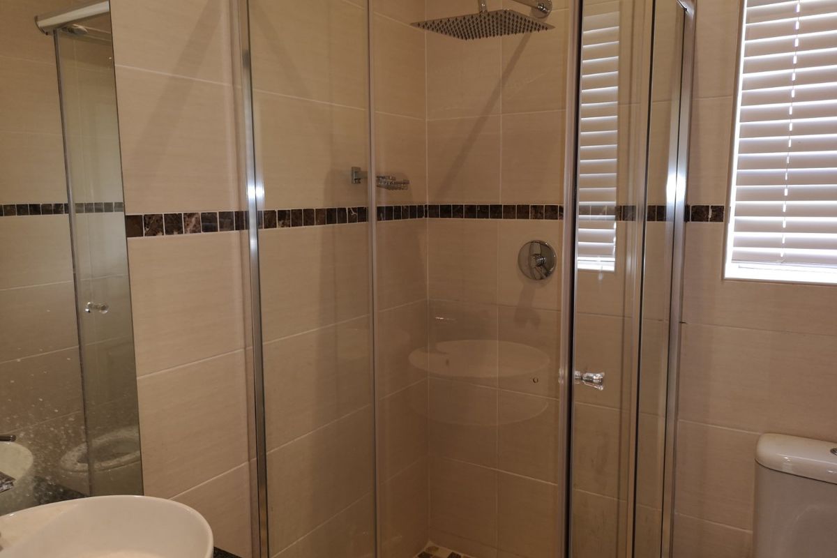 A modern bathroom featuring a glass-enclosed shower with a rainfall showerhead, tiled walls with a decorative mosaic border, and a white toilet.