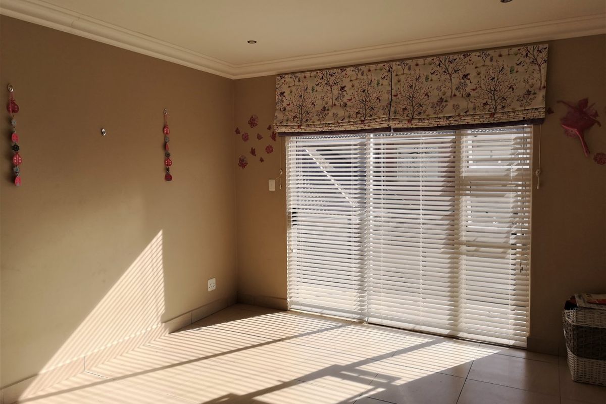 A bright, empty living room featuring tiled flooring, recessed ceiling lighting, and large sliding glass doors fitted with horizontal blinds and a decorative valance.