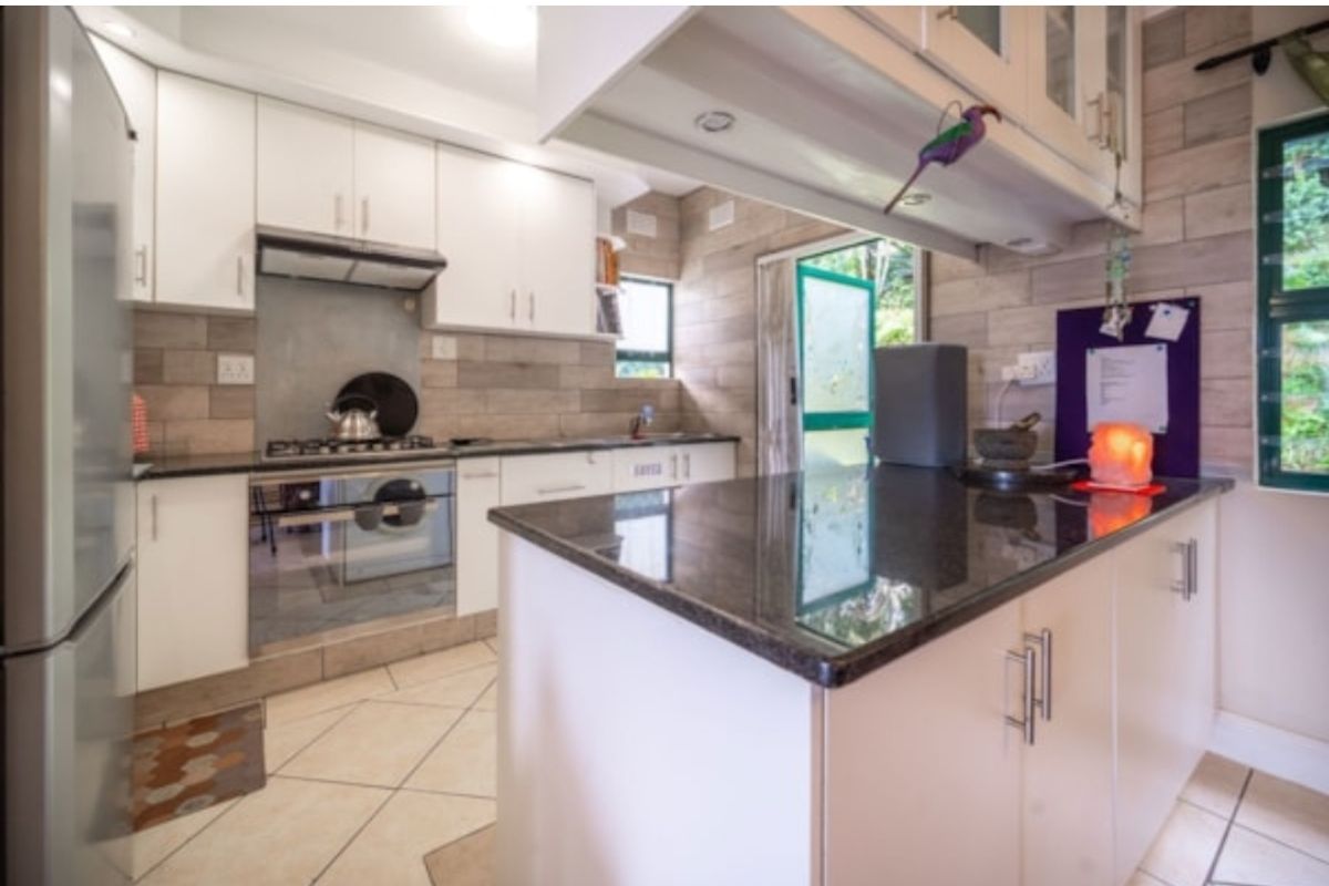 A functional kitchen featuring white cabinetry, dark granite countertops, a built-in gas hob, oven, and extractor fan, with tiled flooring and backsplash.