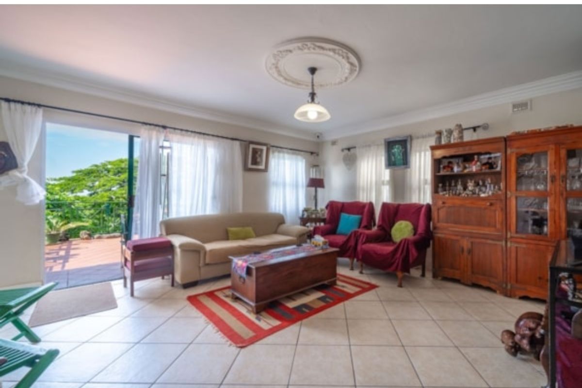 A spacious living room featuring tiled flooring, decorative ceiling rose, and large sliding glass doors that open onto an outdoor patio area.