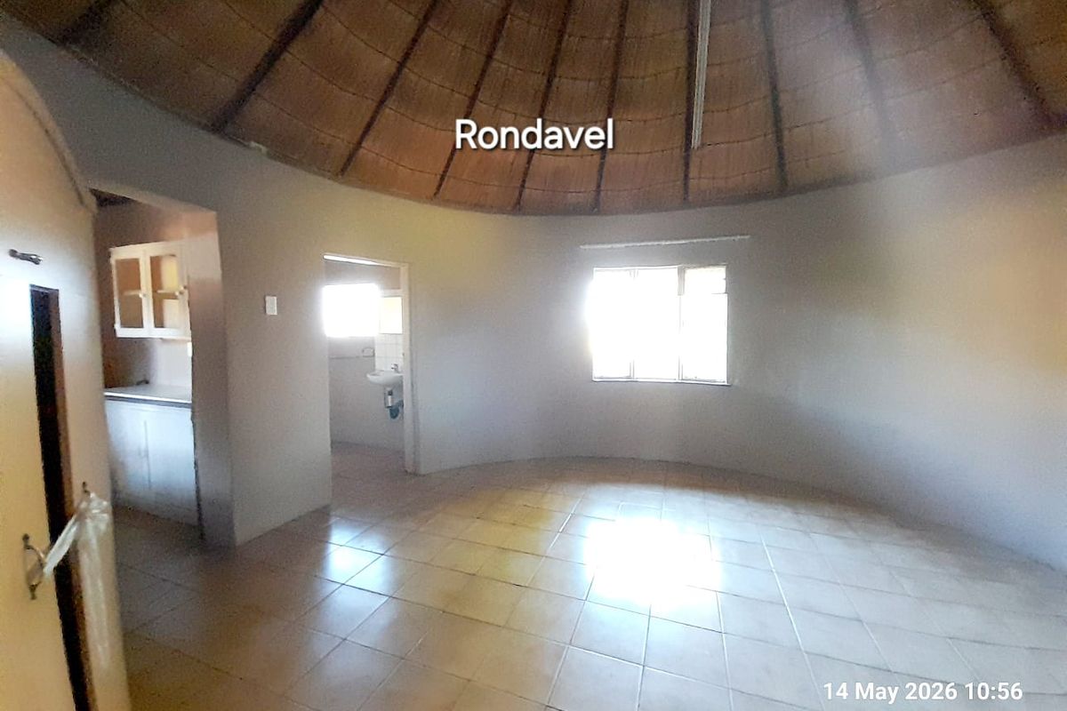Interior view of a traditional rondavel featuring a high thatched ceiling, tiled flooring, and an adjoining kitchenette and bathroom area.