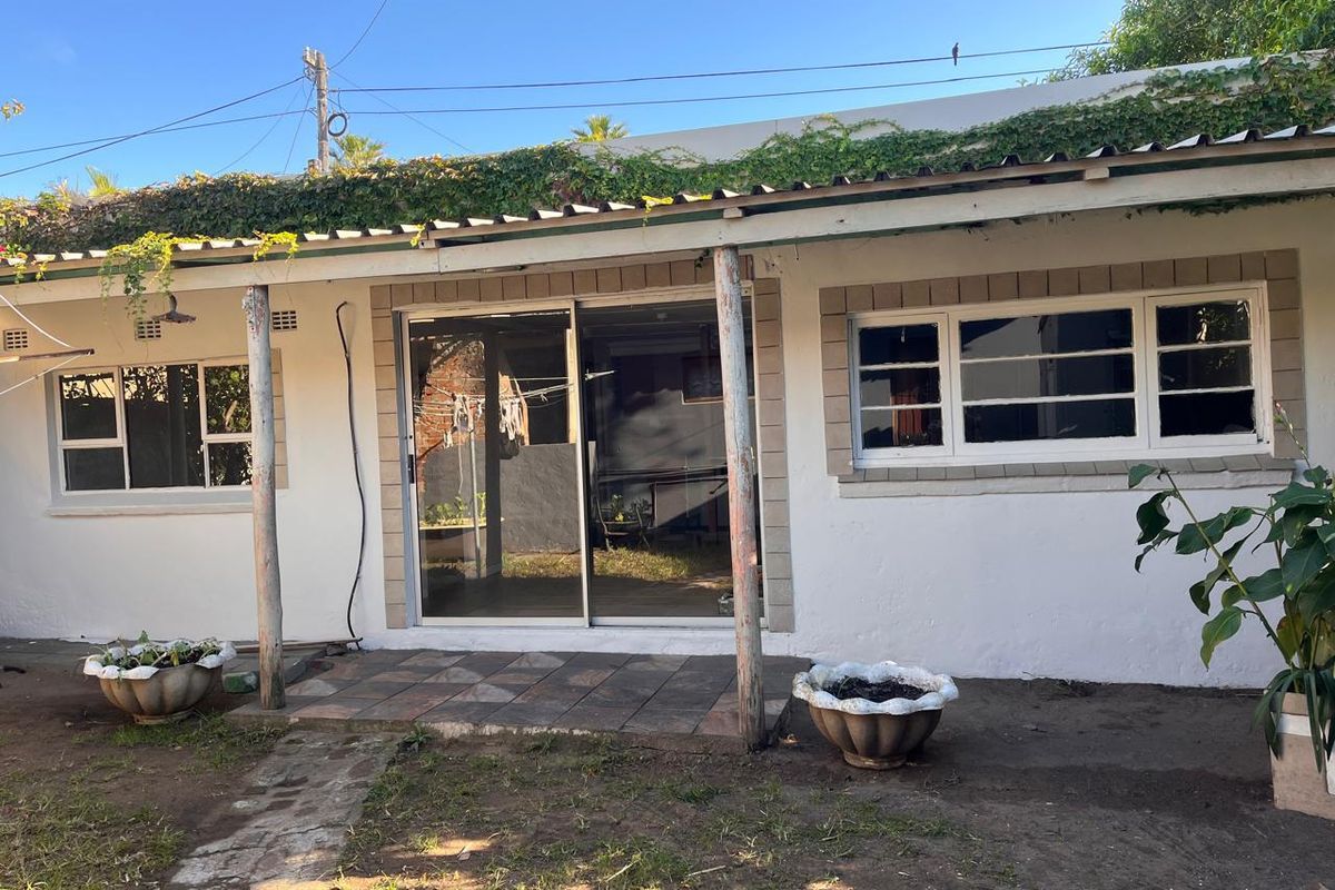 Rear exterior view of the house featuring a tiled patio area, sliding glass doors, and timber support posts under a corrugated roof.