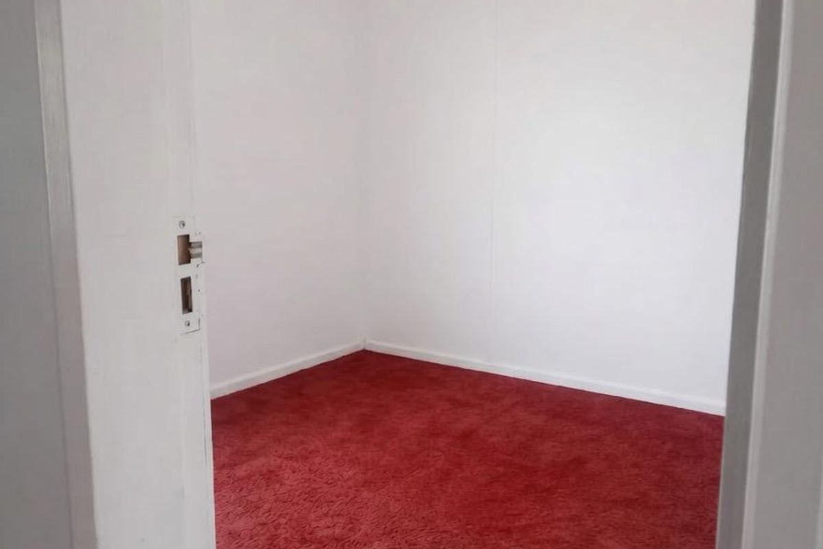 A vacant bedroom featuring red fitted carpeting and white painted walls, offering a blank canvas for potential updates and interior design.