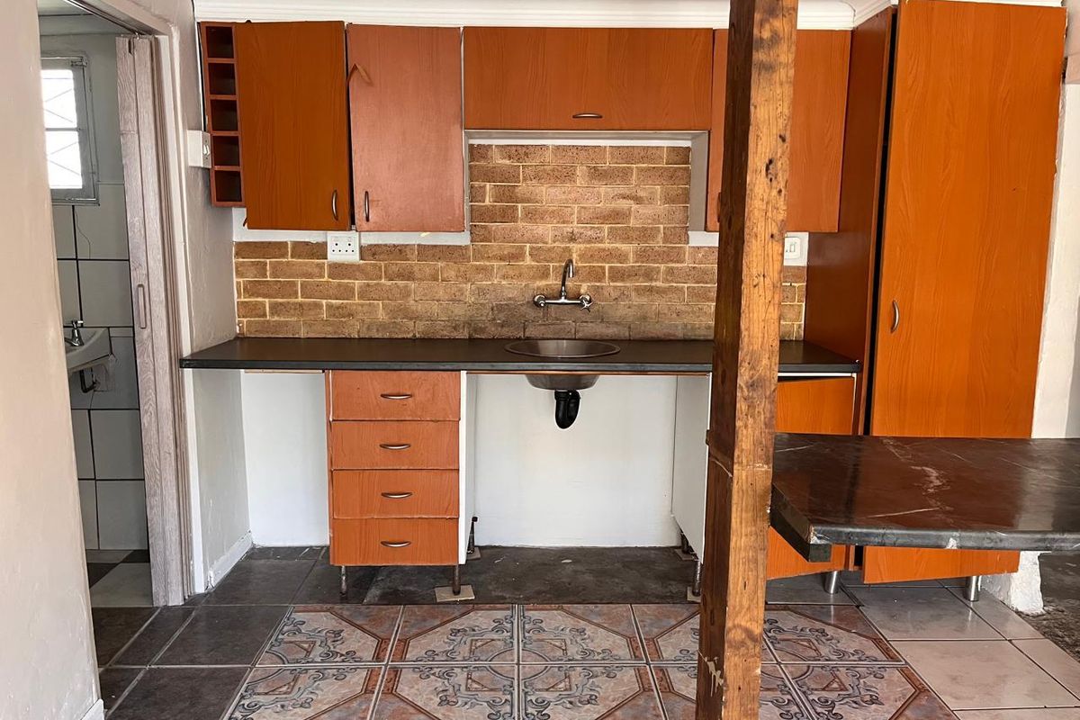 A dated kitchen area featuring wood-look cabinetry, an exposed brick backsplash, and a single stainless steel sink, requiring modernization and cosmetic updates.
