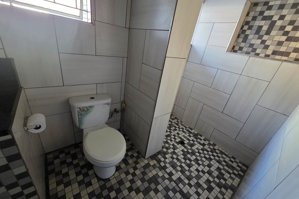 A functional bathroom featuring a walk-in shower area with mosaic floor tiling, wall-mounted toilet, and a window for natural ventilation.