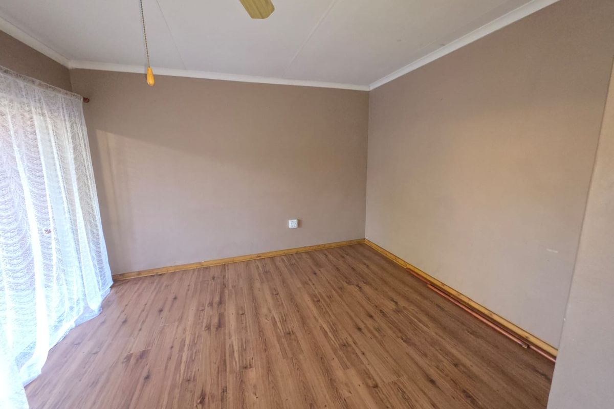 An empty bedroom featuring wood-look laminate flooring, a ceiling fan, and neutral wall tones, offering a blank canvas for personalization.