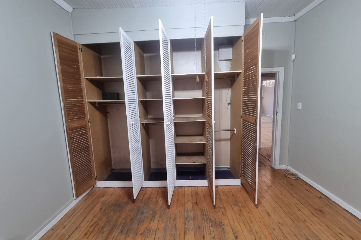 A bedroom featuring original timber flooring and built-in louvered door wardrobes with internal shelving and hanging space.