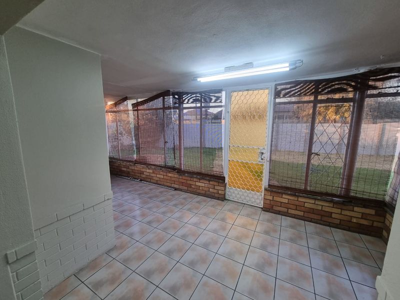 A covered patio area featuring tiled flooring, brick base walls, and security screen doors, providing a functional transition space to the rear garden.