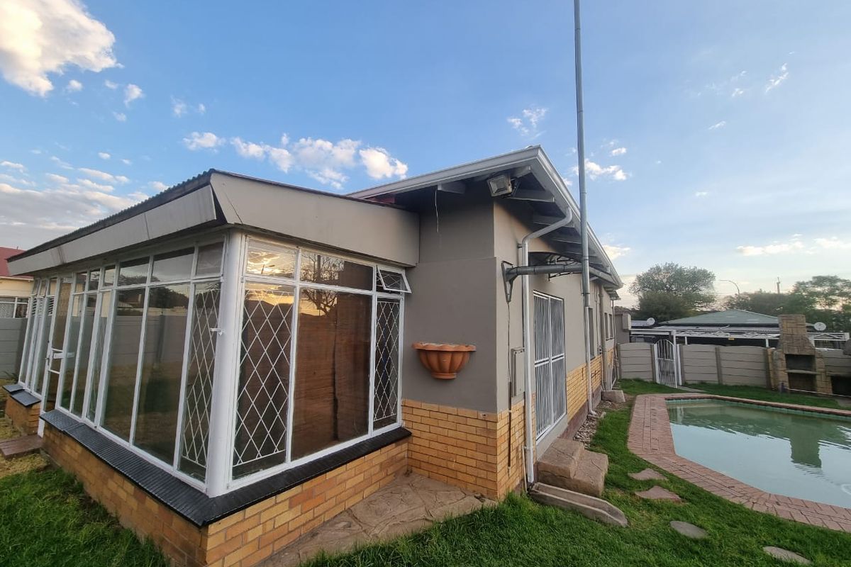 Rear view of the property featuring an enclosed sunroom, a swimming pool, and a built-in outdoor braai area within a private garden setting.