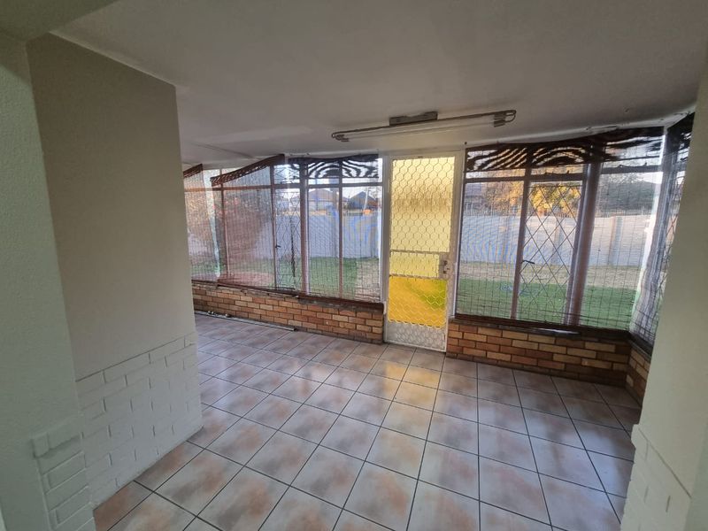 An enclosed patio area featuring tiled flooring, brick base walls, and large windows with security gates, offering a view of the rear garden.