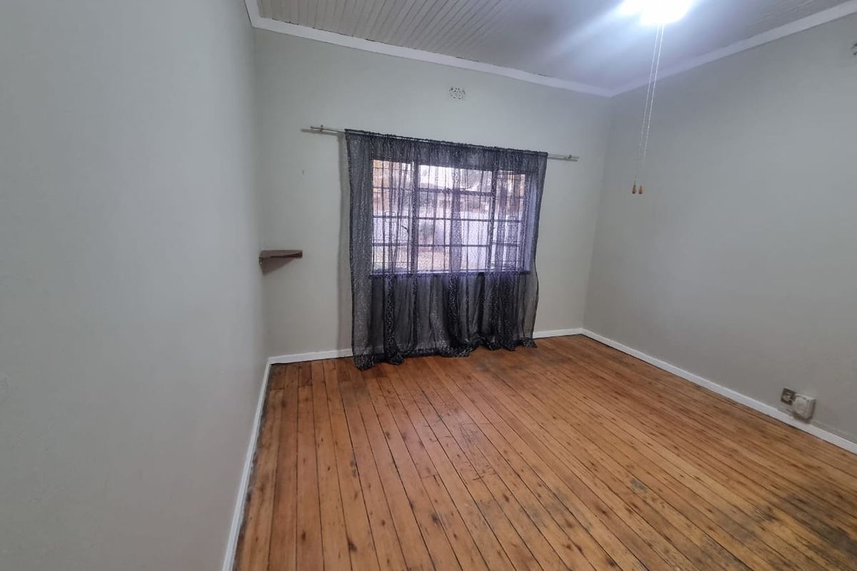 An empty bedroom featuring original timber flooring, a beadboard ceiling, and a ceiling fan, offering a blank canvas for renovation.