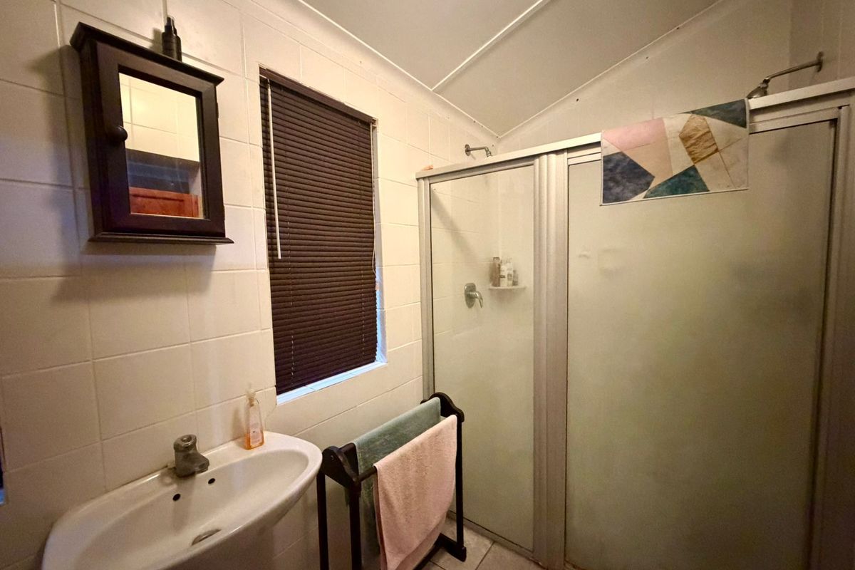 A functional bathroom featuring a pedestal basin, a shower enclosure with a frosted glass door, and tiled walls.