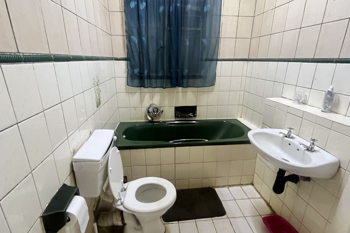 A dated bathroom featuring a green built-in bathtub, wall-mounted basin, and toilet, finished with full-height ceramic wall tiling.