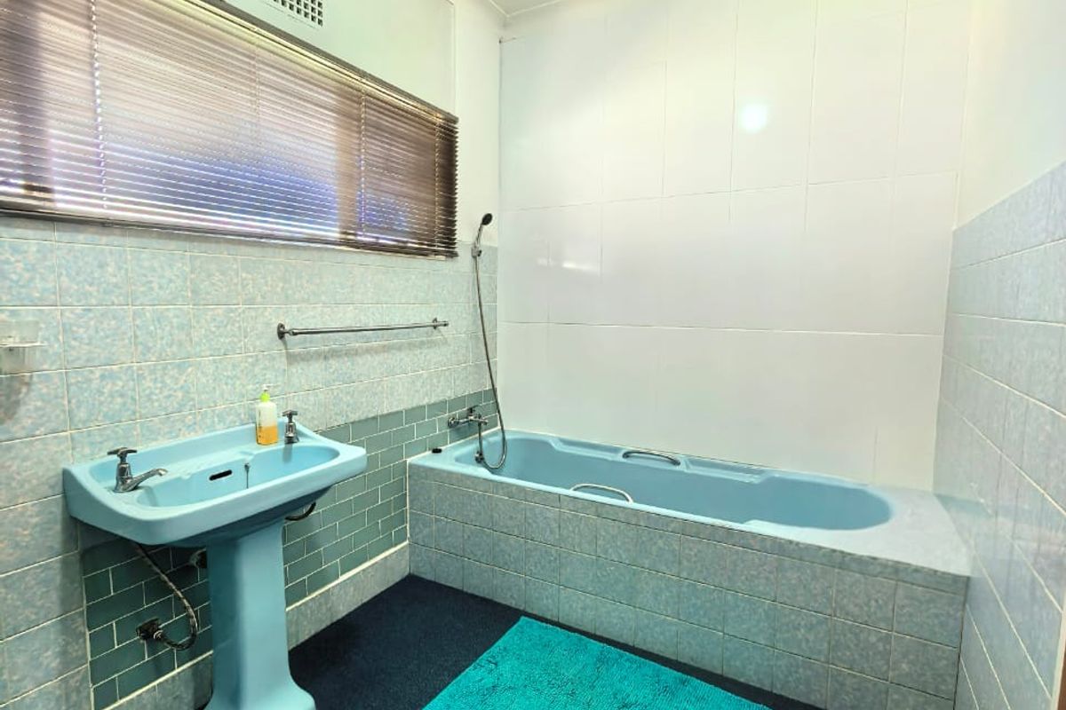 A dated bathroom featuring a blue pedestal basin and matching bathtub, with tiled walls and carpeted flooring.