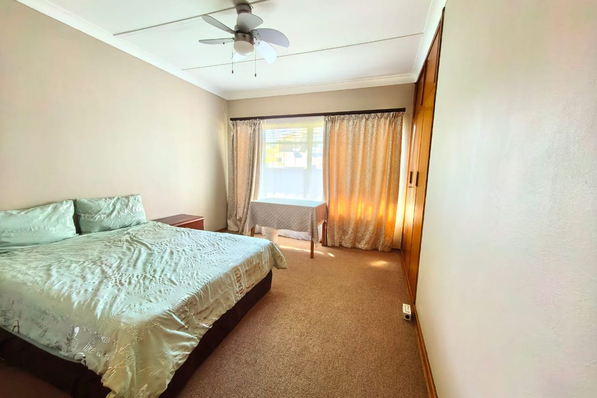 A bedroom featuring built-in wooden cupboards, carpeted flooring, and a ceiling fan, offering a functional and neutral living space.