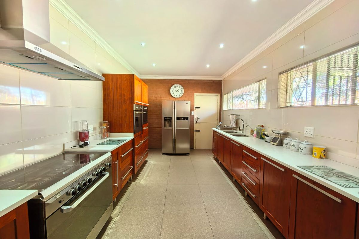 Spacious galley-style kitchen featuring wooden cabinetry, tiled flooring, built-in oven, extractor fan, and ample countertop workspace.