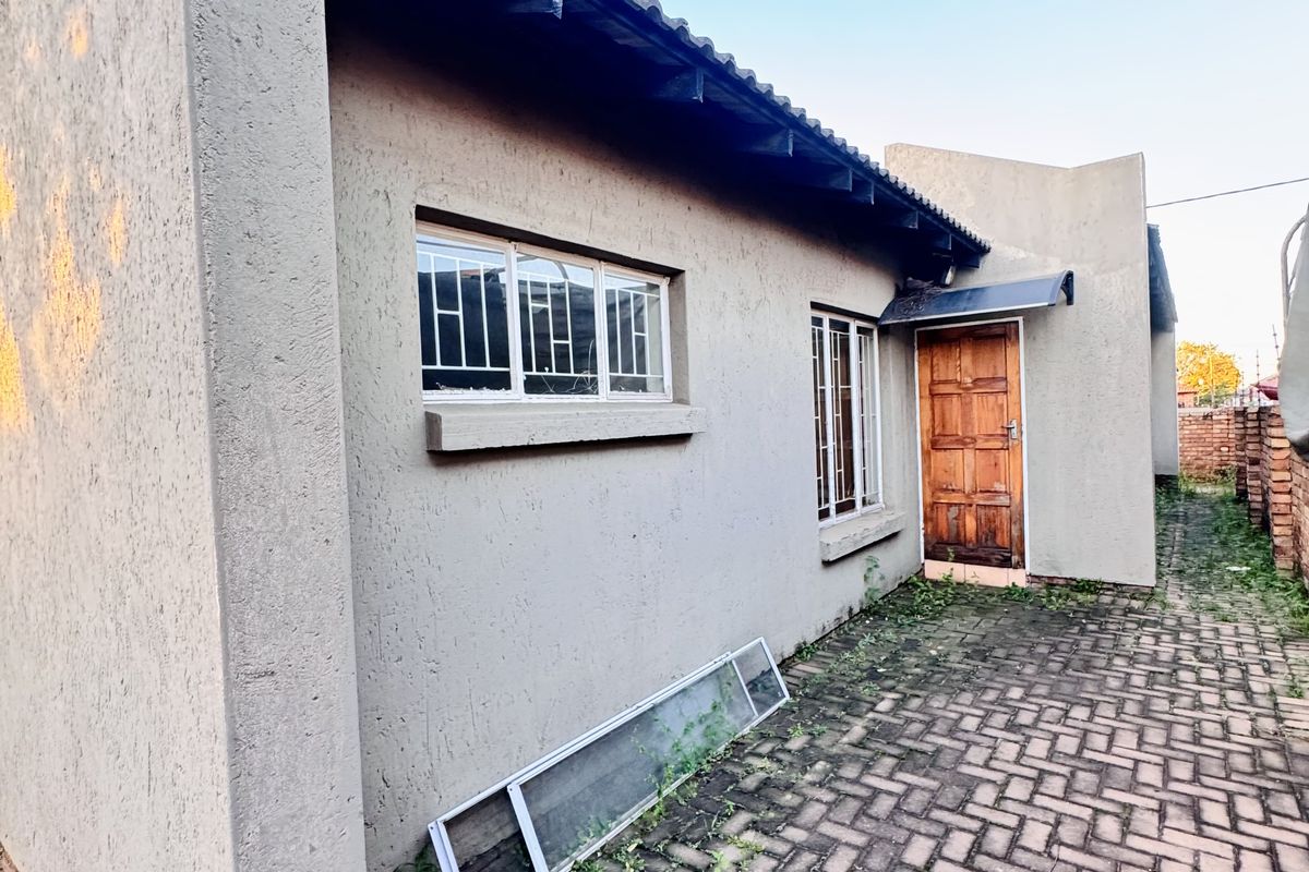Side exterior view of the house featuring paved walkway, timber entrance door, and security bars on windows.