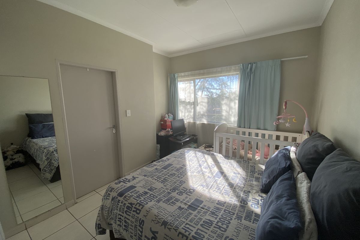 A functional bedroom featuring tiled flooring, a built-in cupboard, and a window with curtain rails, providing a neutral space for personalization.