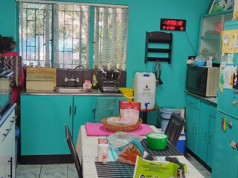 A functional kitchen featuring teal cabinetry, a stainless steel sink, and a compact dining area, offering a practical space for daily meal preparation.