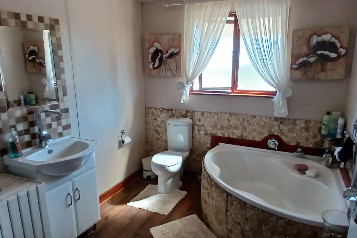 A functional bathroom featuring a corner bathtub with stone-tiled surround, a vanity basin with a mosaic-tiled mirror, and a standard toilet.