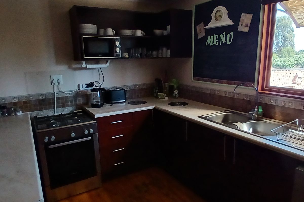 A functional kitchen featuring dark cabinetry, a built-in gas stove with oven, double sink, and tiled backsplash with a view of the garden.