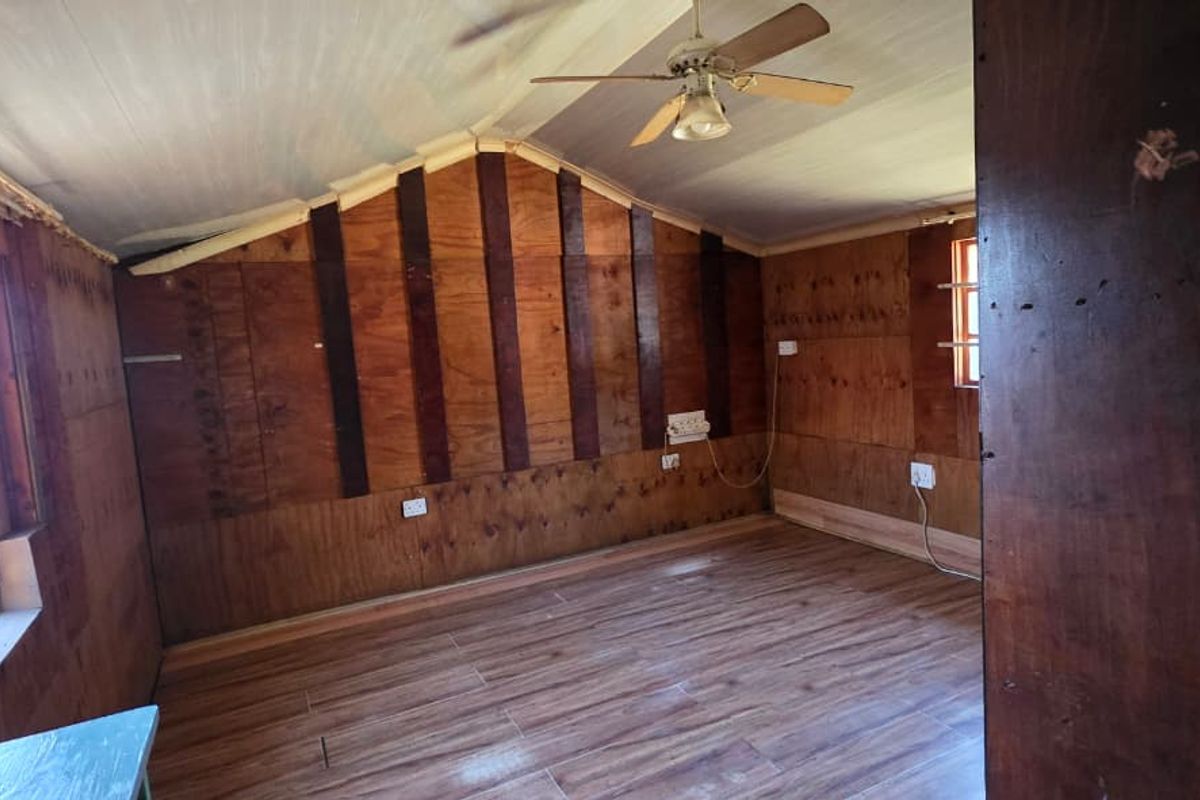 An empty bedroom featuring wood-paneled walls, tiled flooring, and a ceiling fan, offering a rustic aesthetic ready for renovation or personalization.