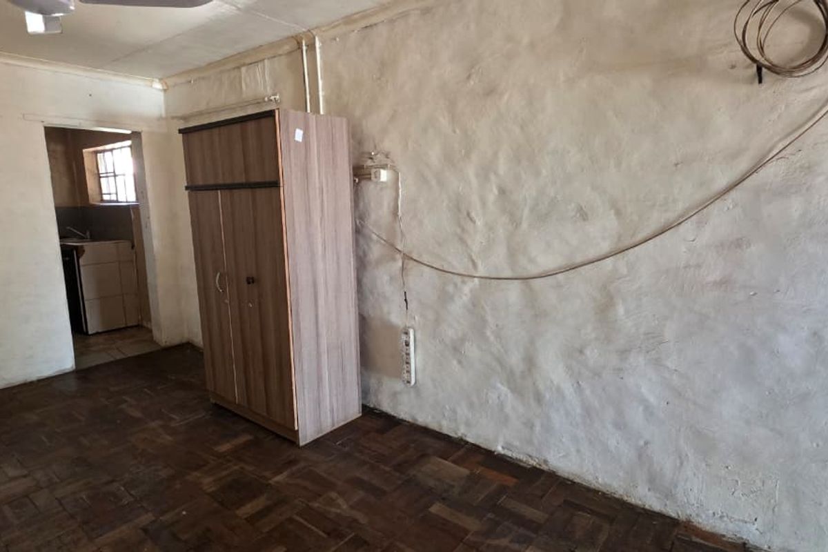 A basic living area featuring original parquet flooring and textured wall finishes, with an adjacent view into a small kitchen space.