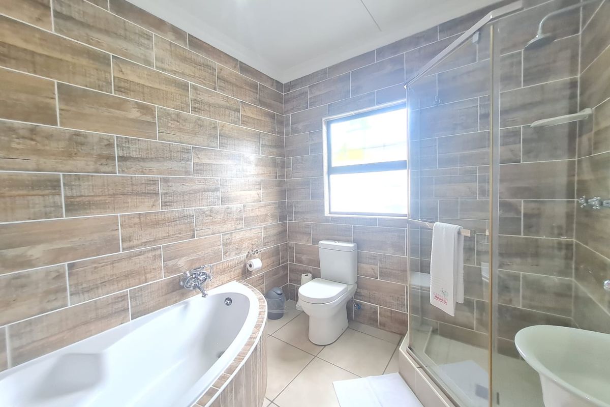 Modern bathroom featuring wood-look wall tiling, a built-in bathtub, a glass-enclosed shower, and a standard toilet.