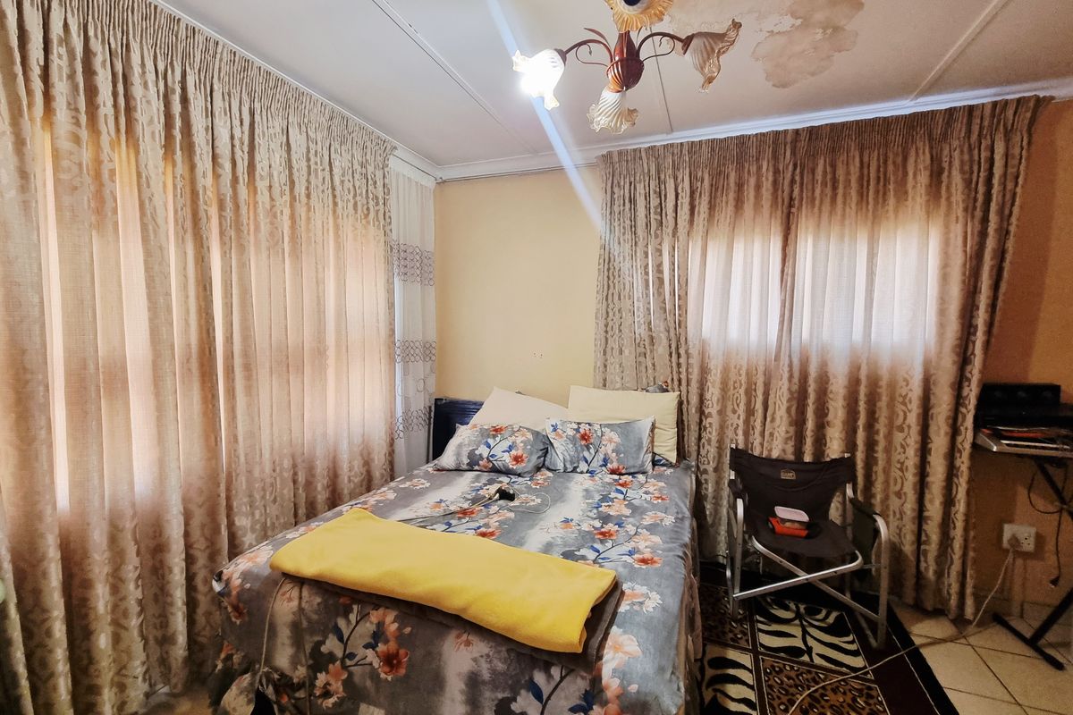 A bedroom featuring tiled flooring, large windows with curtains, and a central light fixture, showing signs of ceiling water damage.