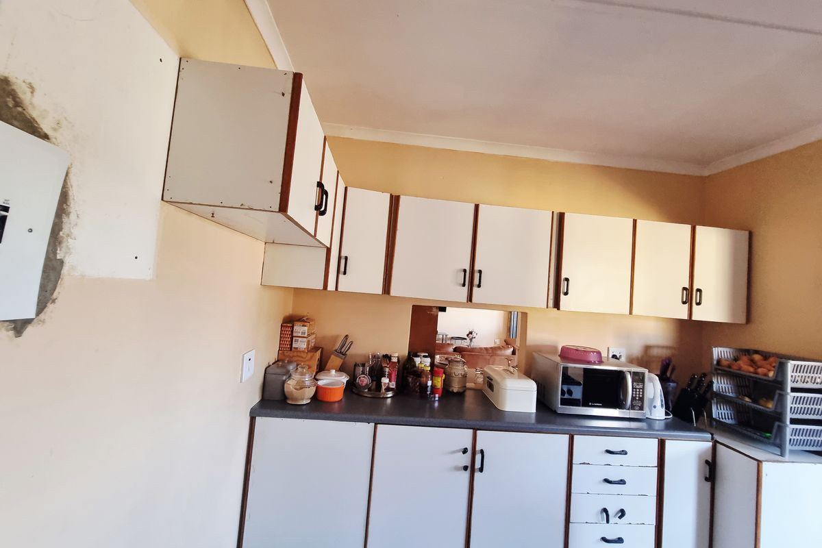 A dated kitchen area featuring white laminate cabinetry, laminate countertops, and a built-in microwave space, requiring cosmetic updates.