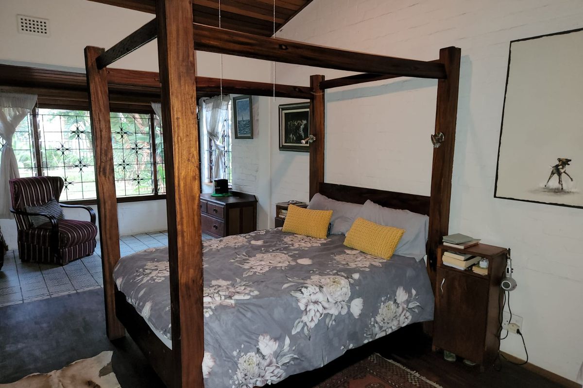 Spacious bedroom featuring a high timber-paneled ceiling, exposed brick walls, and large windows with security grilles, offering a rustic and character-filled living space.