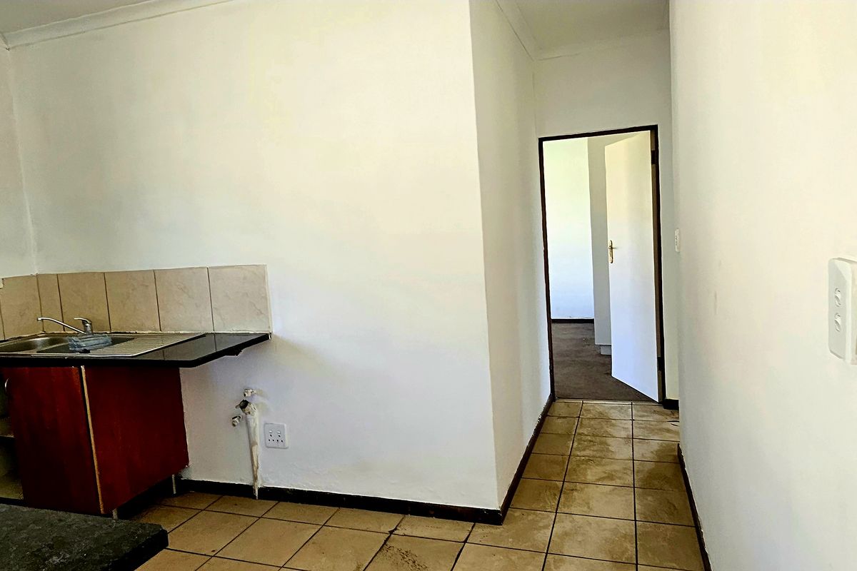 A compact kitchen area featuring built-in cabinetry, a stainless steel sink, and tiled flooring, currently vacant and ready for renovation.