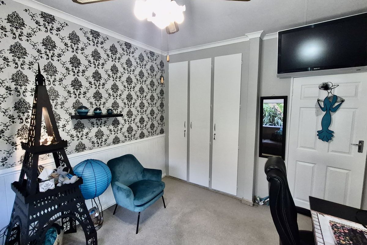 A bedroom featuring built-in wardrobes, decorative wallpaper, and a ceiling fan, offering functional storage and a distinct aesthetic.