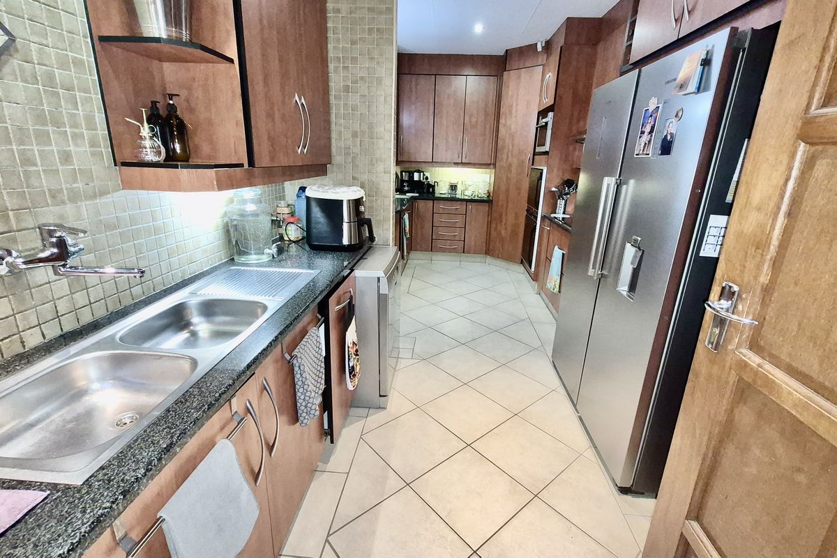 A functional kitchen featuring wood-veneer cabinetry, granite countertops, double stainless steel sink, and tiled flooring in a galley-style layout.