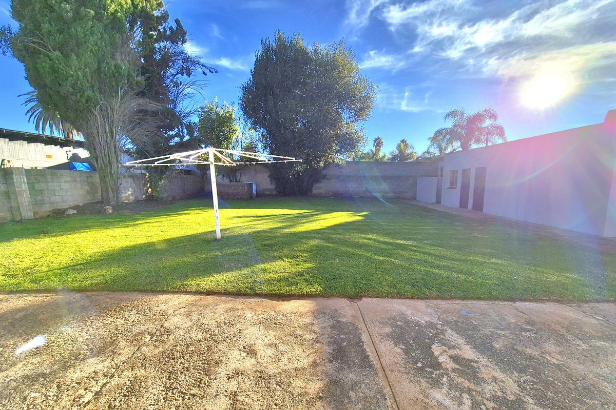 Spacious rear garden featuring a large lawn area, perimeter boundary walls, and a paved patio section.