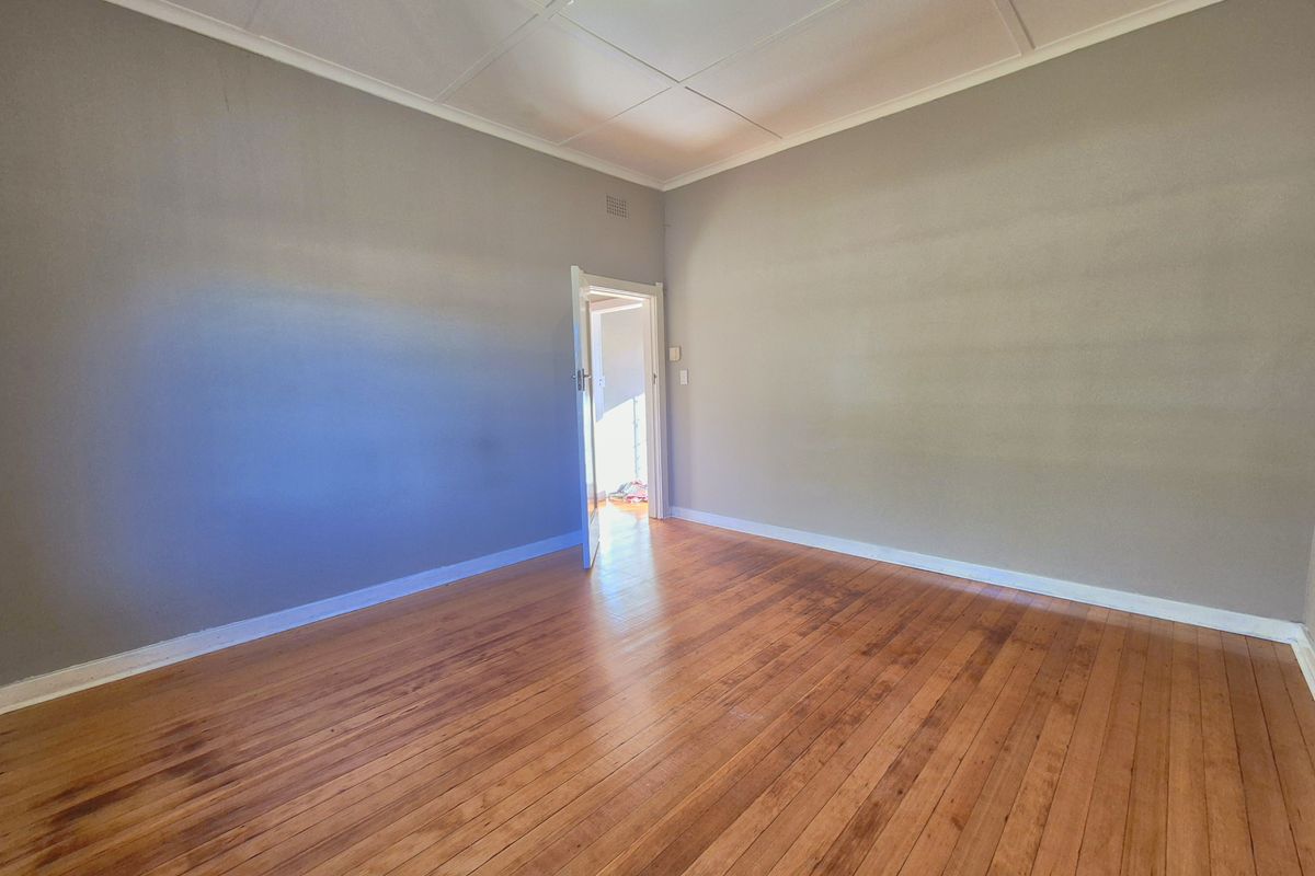 A spacious, empty bedroom featuring polished timber flooring, neutral wall tones, and a classic ceiling design with a central light fixture.