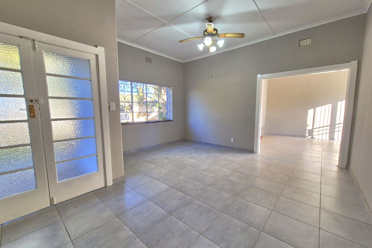 A bright, empty living room featuring neutral tiled flooring, a ceiling fan, and glass-paneled double doors leading to the exterior.